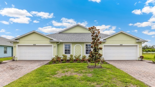 Outside of the Carrington model. Green home with two windows, two garages, two front doors. Two grey paver driveways.