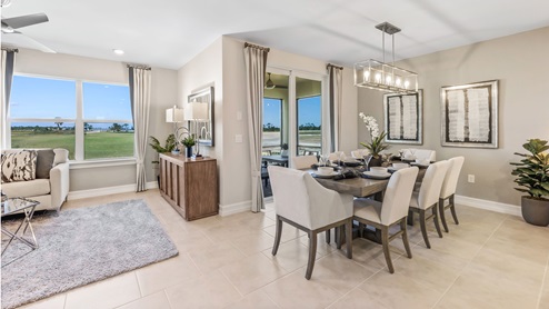 Inside of the Cali model dining room. Tile flooring and white walls. Dining room has a six-person dining table with hanging light fixture above it. Kitchen can be seen in the background.