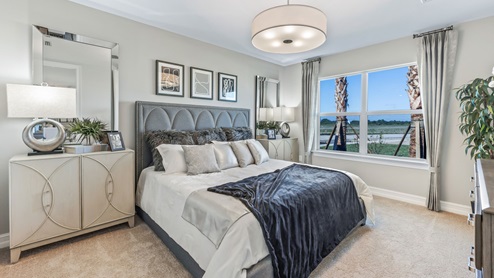 Inside of the Cali model bedroom one. Crème carpet with white walls. Room contains bed with nightstand on either side as well as a dresser on the opposing wall. Room also has window.