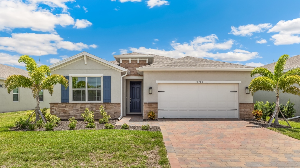 Outside of the Delray A model. White home with two car garage, two windows with shutters, and front door. Mixed paver driveway.