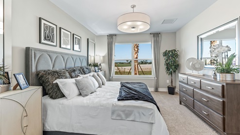 Inside of the Cali model bedroom two. Crème carpet with white walls. Room contains bed with nightstand on either side as well as a dresser on the opposing wall. Room also has window.