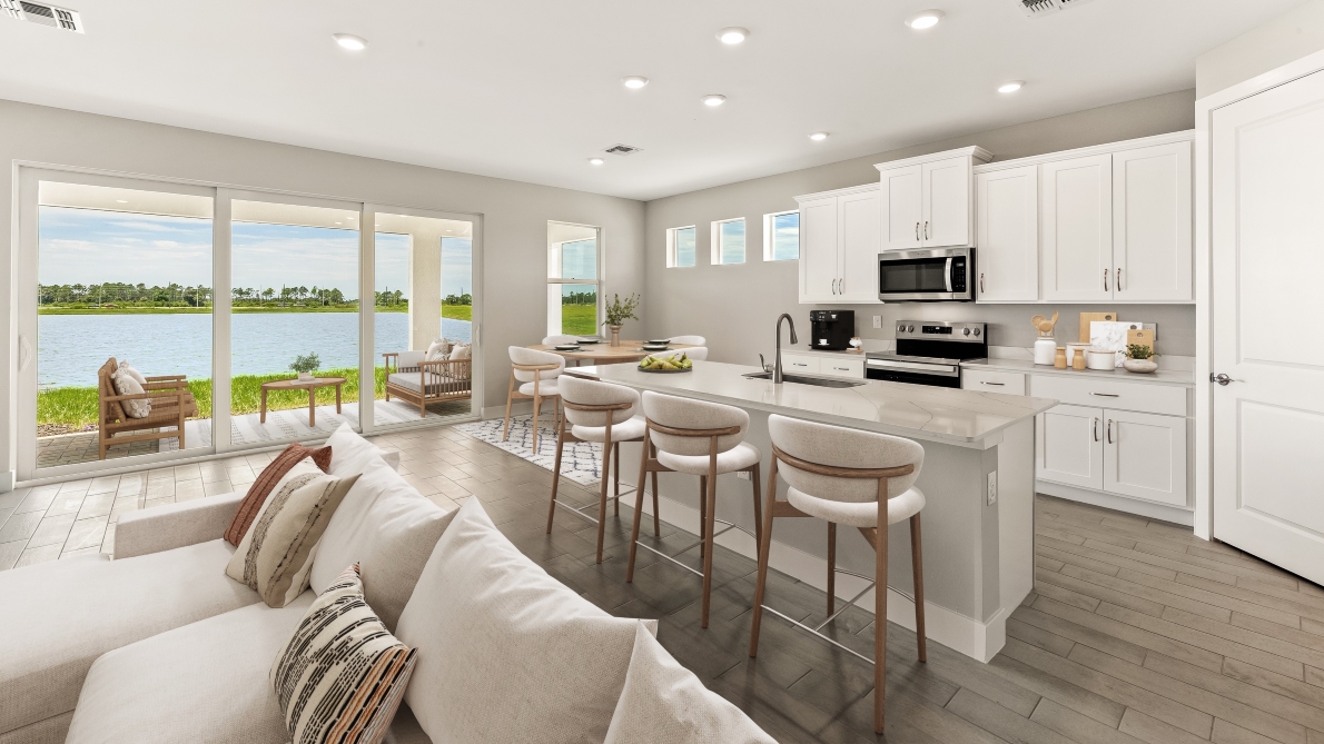 Inside of the Shelby model home Kitchen with stainless steel appliances. Living room couch from this angle and patio sliding doors to outside dining area.
