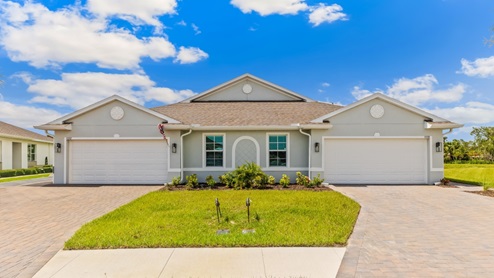 Exterior elevation of white home with two garages, white trim and light tan paver driveways.