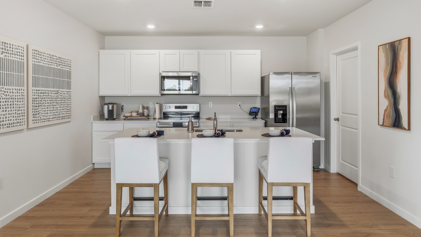 Inside of the Carrington model kitchen. Stainless steel appliances, three barstool chairs.