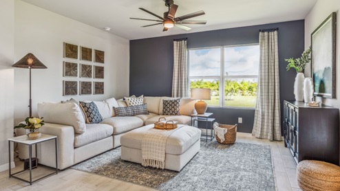 Inside of the Cali model living area. Wood tile flooring and teal walls. Living area contains two couches, an ottoman, storage shelf, and small table. Room also contains a window.