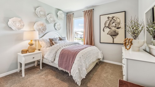 Inside of the Cali model bedroom 2. Crème carpet with one off-white wall and one teal wall. Room contains one bed, a nightstand on one side, and a dresser on the opposing wall. Room also has a window.