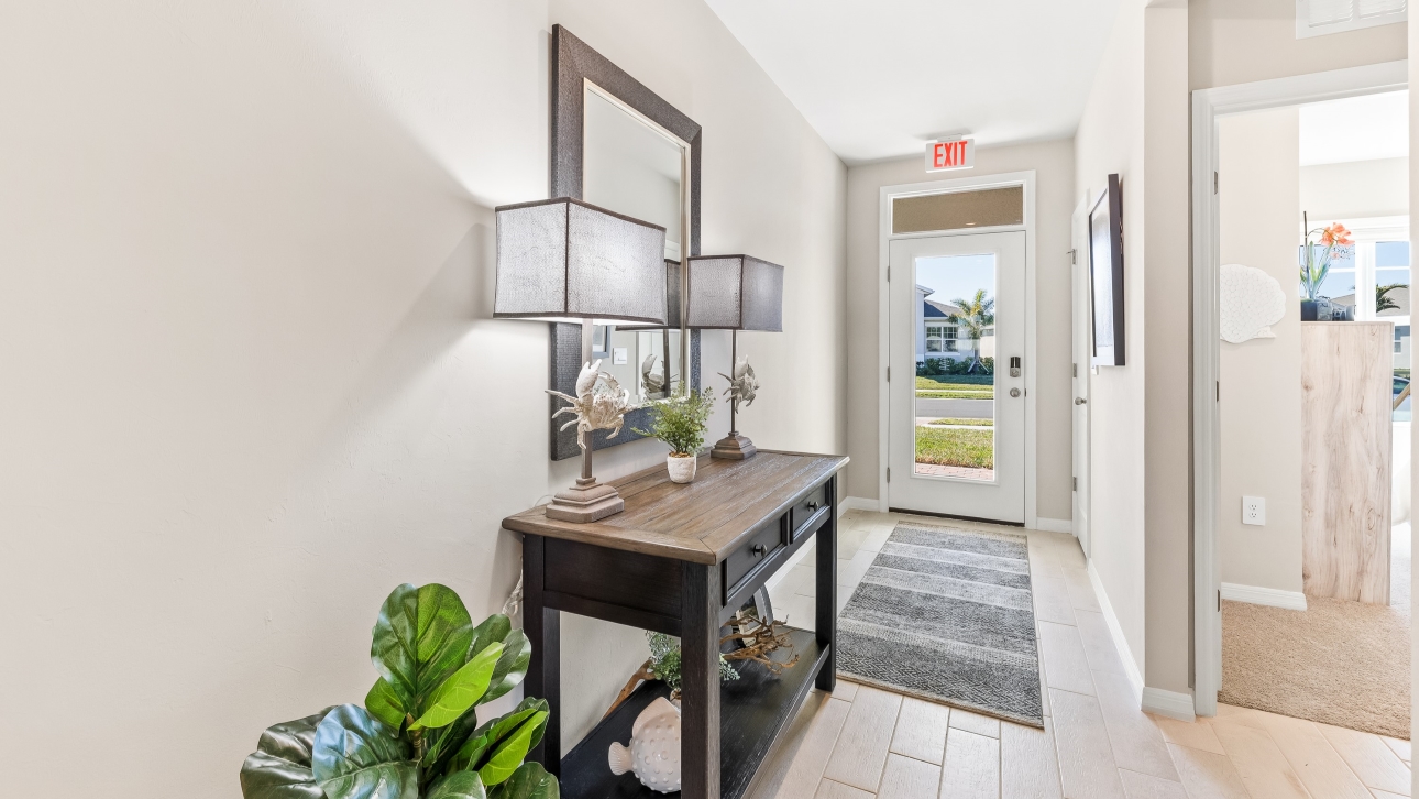 Inside the entry way of the Cali model. Grey plank tile floors and off-white walls. Front door hallway and access to rooms.