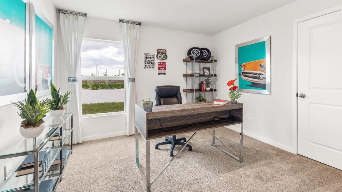 Inside of the Jemison model den. Grey carpet with off white walls. Room contains a desk with a desk chair and a shelf table on the other wall. Room also contains a window.