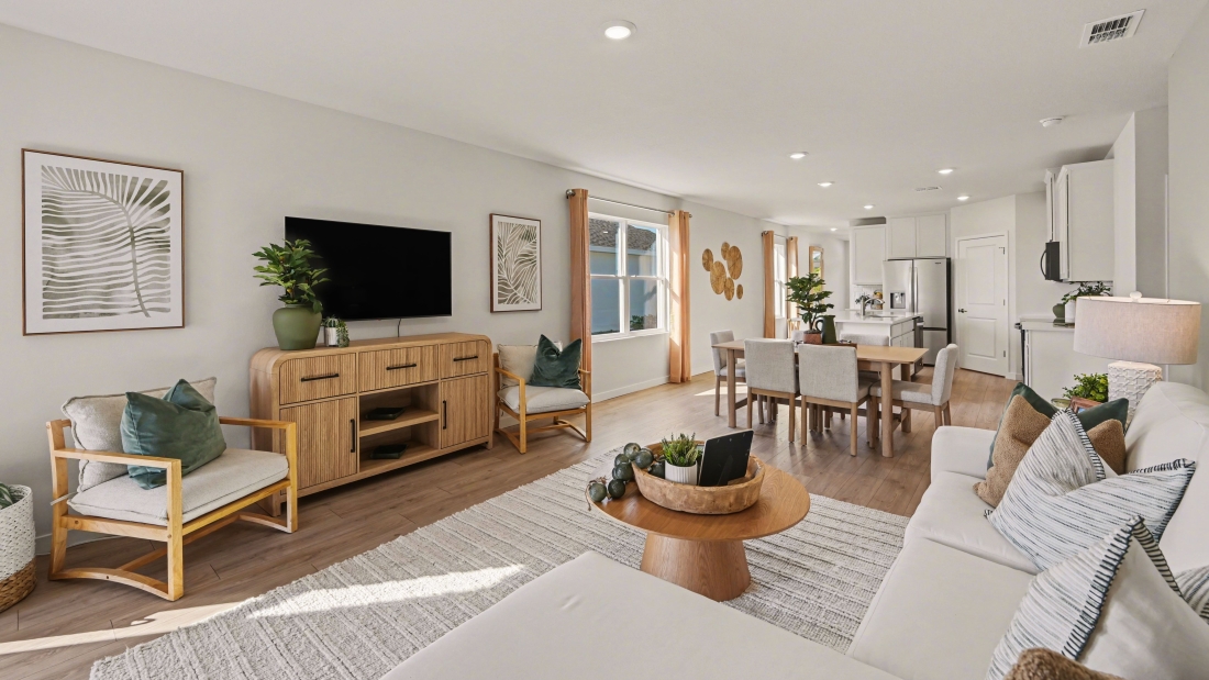 Inside of the Harper model in Central, FL. Living room with couches and tv. You can see the Dining room and Kitchen and Entry door from this angle of the house.