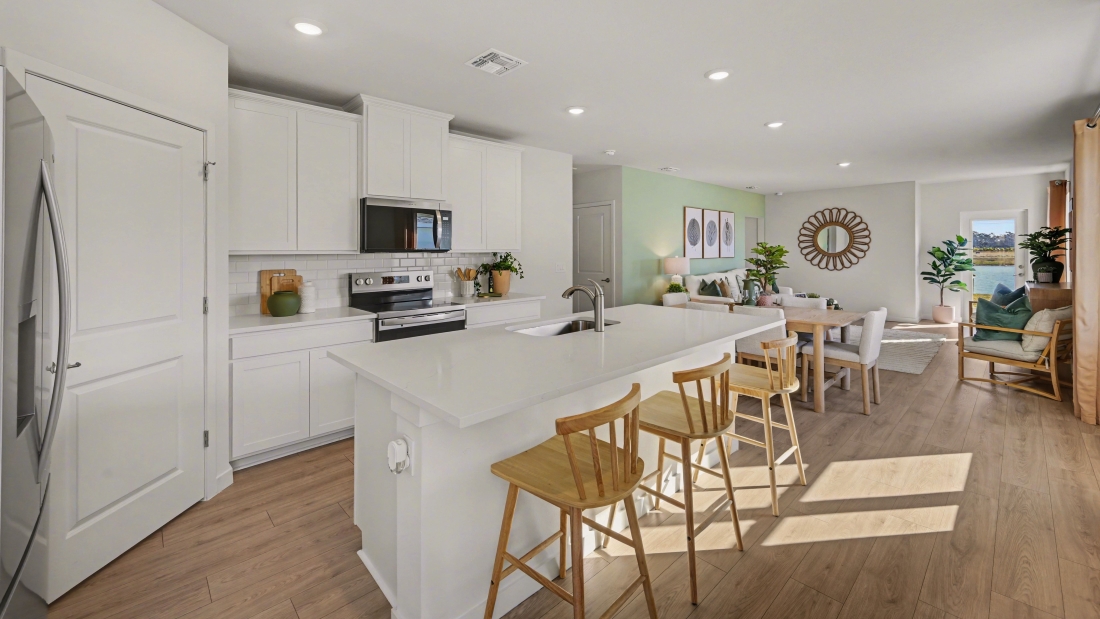 Inside of the Harper model in Central, FL. Kitchen with stainless steel appliances and island with bar seating. Dining area visible here with and living room towards the back.