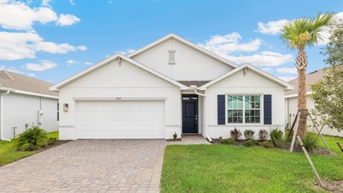 Outside of the Cali model C home. Blue home, two car garage, window with shutters, and front door. Mixed paver driveway.