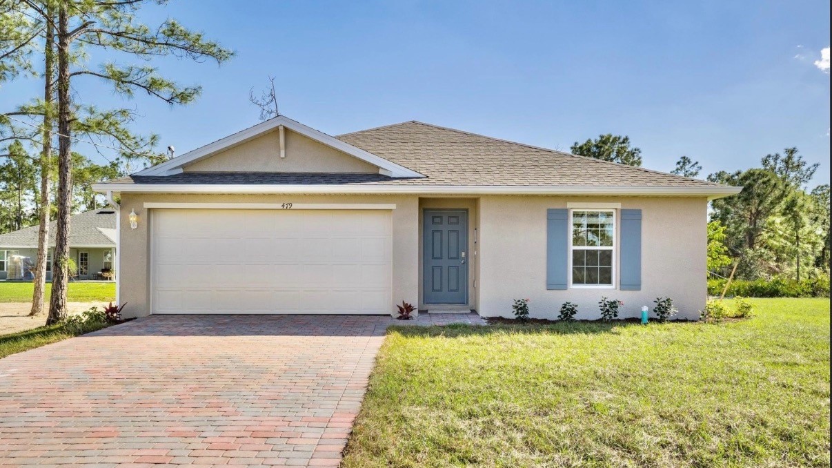 Outside of the Freeport II model. White home with a front door, two car garage, window with shutters, and a light paver driveway.