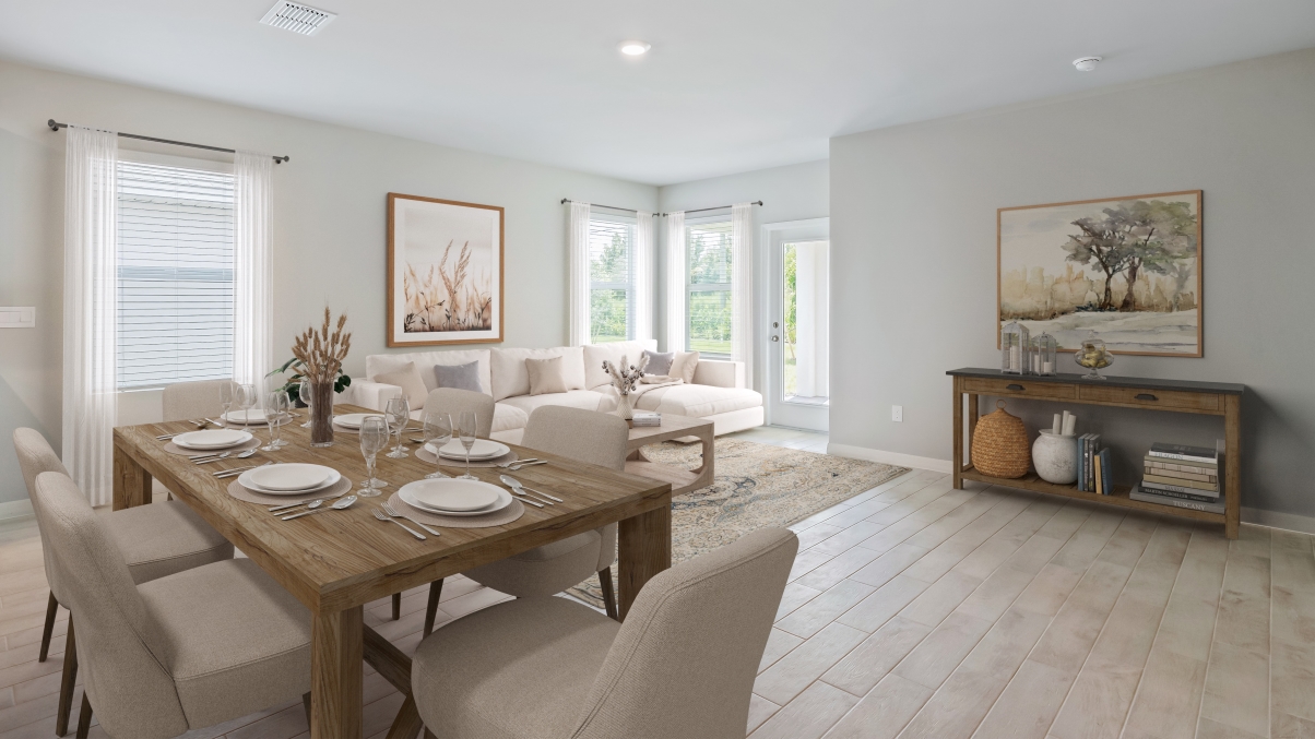 Inside the Lakeside dining room with larger view of the living room and book nook. Dining table is wooden with plushed seating for 6 people. Living room couch is white and furniture is all wood. There is a painting on the wall.