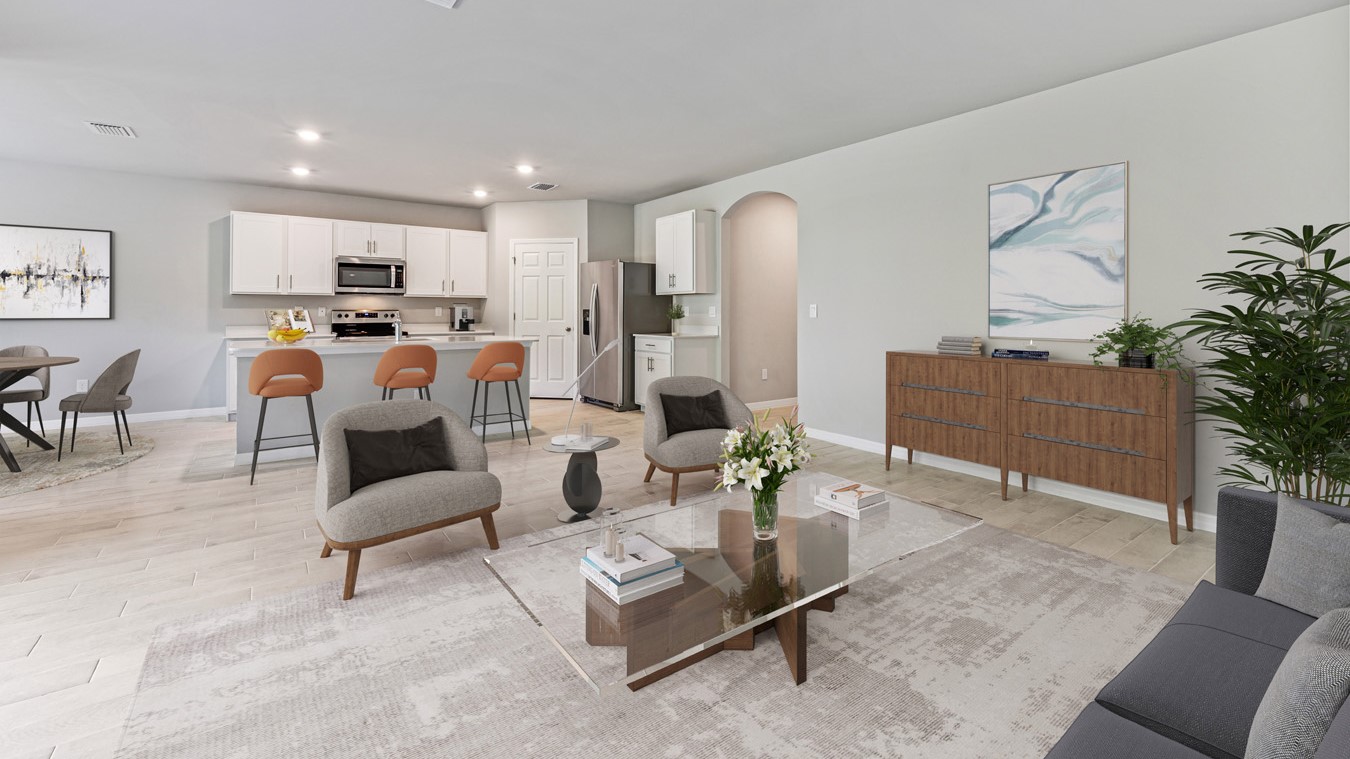 Inside of the Madison living room. Plank tile flooring with off-white walls. Room contains two armchairs with small table between them, wooden storage shelf, coffee table, and small couch. Photo demonstrates that the living room opens up to the kitchen, dining room, and hallway that connects to the front door.
