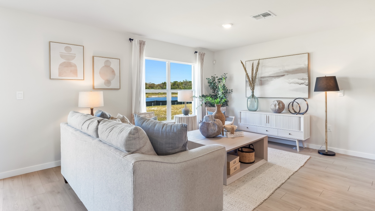 Inside the living room of the Archer model. Contains a couch, coffee table, TV stand, Lamp, and side chair.