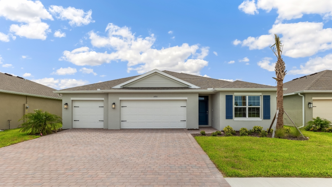 Outside of the Denham model G home. Light home, three car garage, one window with a shutter and front door. Mixed paver driveway.