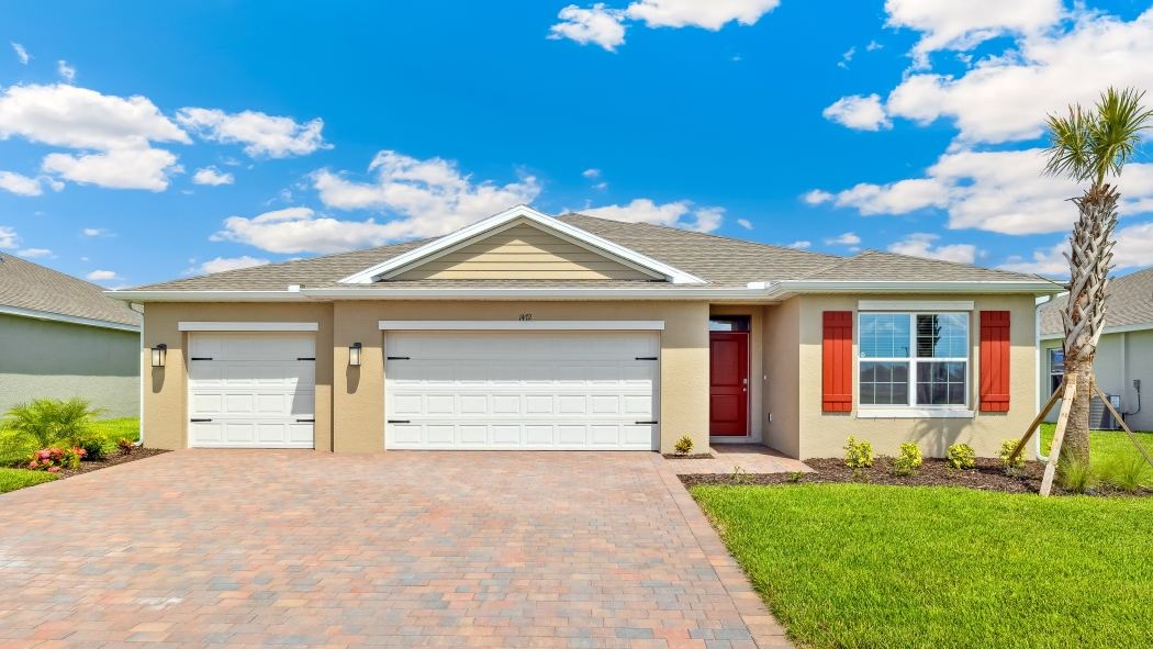 Outside the Denham G model. Beige home with three car garage, teal door, a window with decorative shutters, and mixed paver driveway.