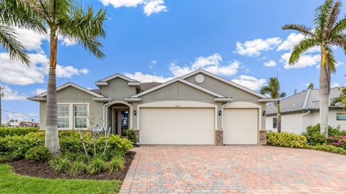 Outside of the Destin model. Green home with two car garage, front door, and window in the front. Mixed paver driveway.