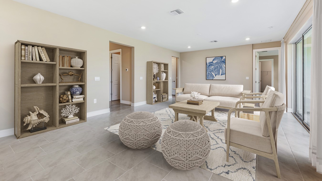 Inside the Kellen model Great Room from infront of the ottomans and seating arrangment. There is also a the large couch. You can see the other side of the room with two large book cases and the halfway to the other bedrooms and laundry room. Tiled throughout.