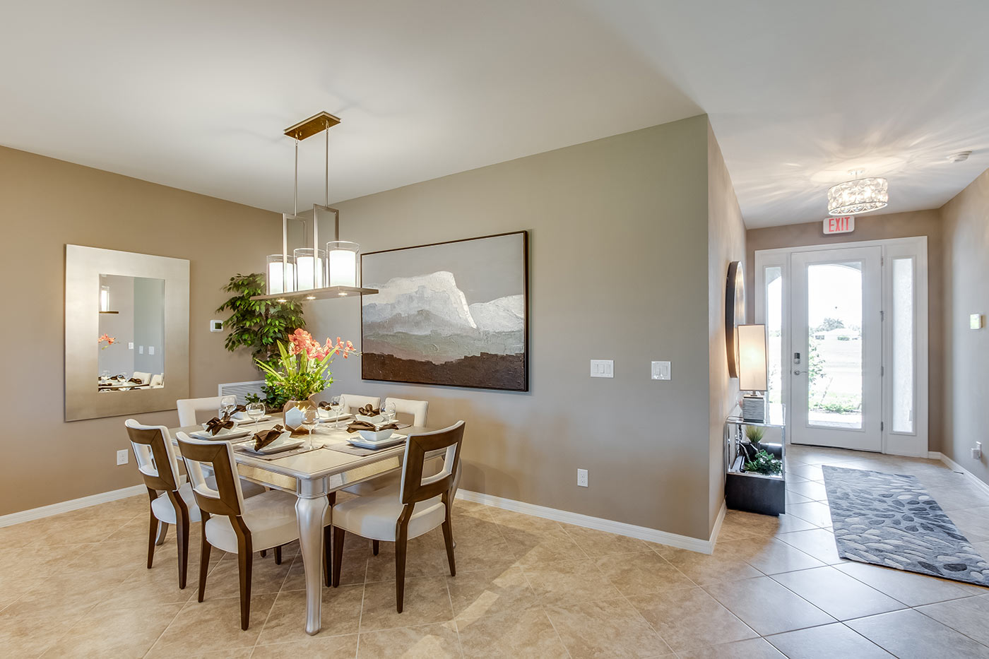 Inside of the Destin model dining room. Tile flooring and off-white walls. Dining are has a six-person dining table and hanging light fixture. In the background the front door can be seen.