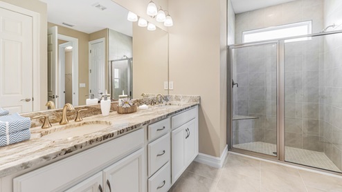 Inside the Kellen model Master Bathroom with dual sinks and shower with no tub, but a seat. Counter tops are marble and cabinetry is white with silver fixings.