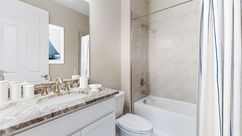 Inside the Kellen model second Bathroom with single sink and shower with tub. Counter tops are marble and cabinetry is white with silver fixings.