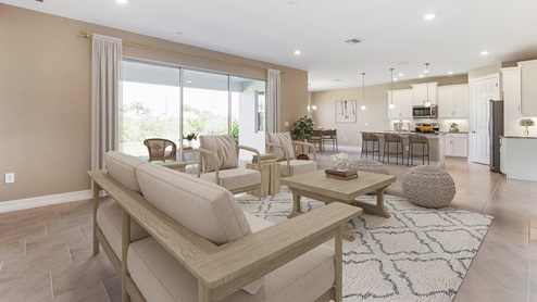 Inside the Kellen model Great Room from behind the large couch. You can see the patio sliding doors, full kitchen and dining area from here. Tiled throughout.