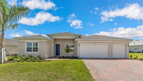 Outside of the Kellen model. Beige home with two car garage, front door, and two windows in the front. Mixed colors paver driveway.