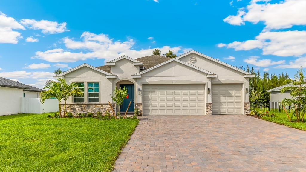 Outside of the Destin model. Beige home with three car garage, front door, and window in the front. Mixed paver driveway.