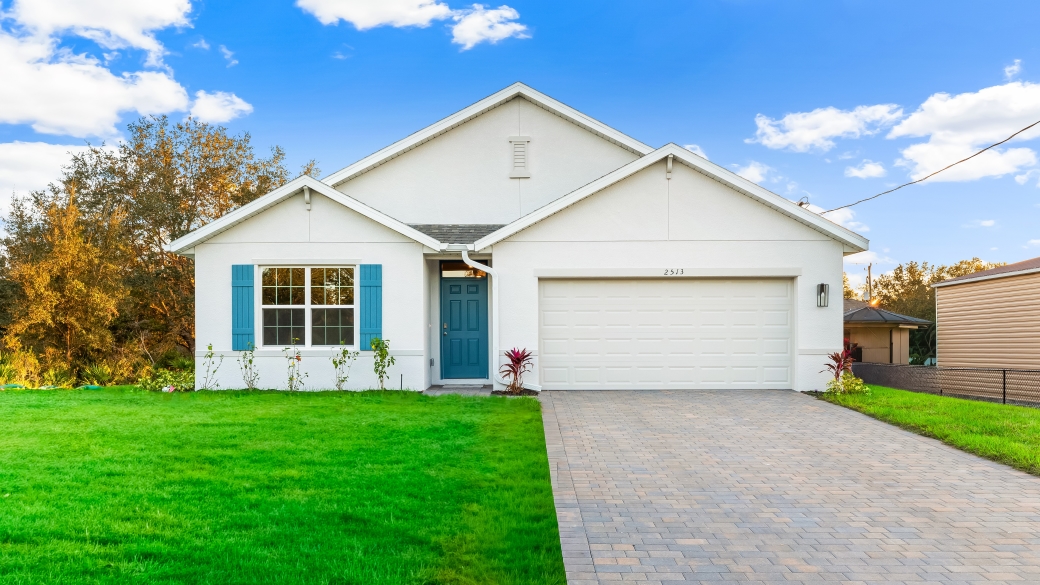 Outside of the Cali D model. White home with two car garage, window with shutters, front door. Mixed paver driveway.