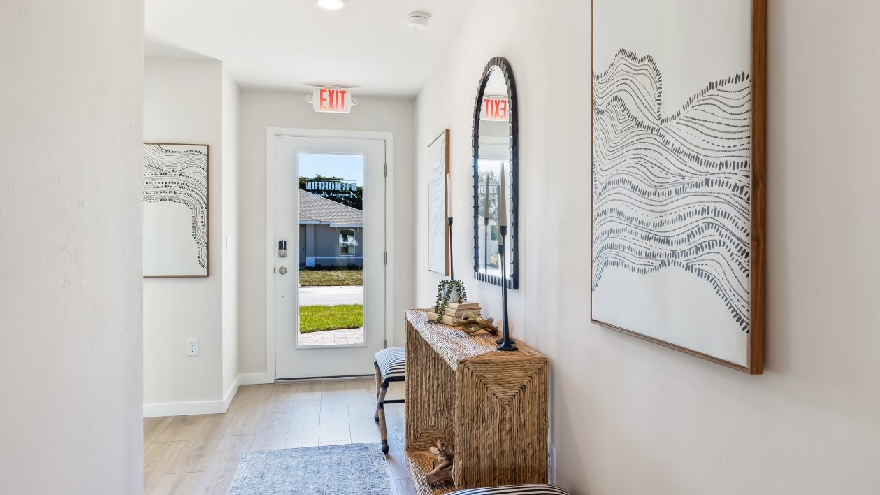 Inside the front door of the Archer II model. Revwood floors with white walls, an entry table, mirror, and small bench.