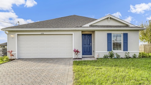 Outside of the Boardwalk A model. Gray home with a two car garage, small window with shutters, and front door. Brown paver driveway.