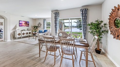 Inside of the Cali model dining room. The dining room contains a six-person dining table and chairs. The living room can be seen in the background as well as the sliding glass door that leads to the back patio.