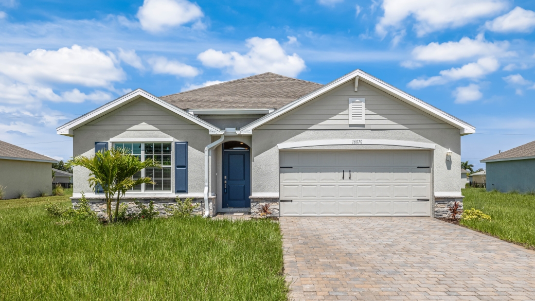 Outside of the Cali model home. Gray home, two car garage, window with shutters, and front door. Mixed paver driveway.