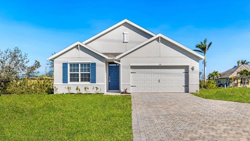 Outside of the Cali D model. Grey home with a two car garage, one window with shutters, and front door. Mixed pavers driveway.