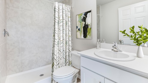 Inside of the Boardwalk model bathroom. Off-white walls, grey tile, white countertops with silver hardware. White toilet as well as white bathtub shower combo.