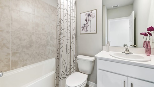 Inside of the Madison bathroom two. White countertops and white cabinets with silver hardware. White toilet. White bathtub with silver shower combo.