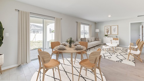 Inside of the Freeport dining room. Dining room has grey wood tiles and creme walls. Dining room contains a four-person round table as well as a connection to the outdoor patio. The photo also demonstrates how the dining room is connected to the living room.