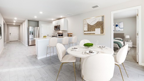 Inside of the Boardwalk kitchen. This photo demonstrates how room one connects to the dining area. Dining area contains four-person round table. Three chairs are behind the table and pulled up to the bar. Grey wood tile floors with off-white walls.