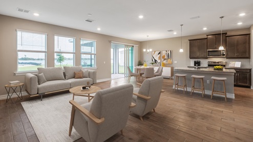 Inside the Coral home, you can see the kitchen, dining room, and living room from here. Cabinets are dark wood and floor is wood tiling. You can see out to the patio from here through 2 windows and a set of sliding doors.