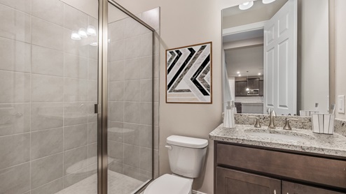 Inside the Coral third bathroom with single sink, dark wood cabinets and a shower next to the toilet.