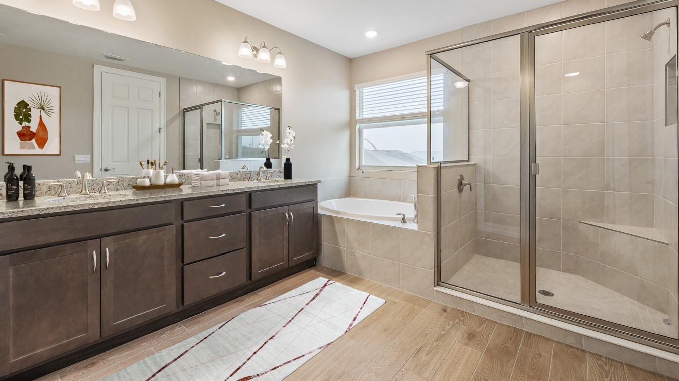 Inside the Coral primary bathroom with dual sinks and dark wooden cabinetry. The shower is tiled with glass/metal doors and the bathrub is next to the shower. Fixtures are stainless steal.