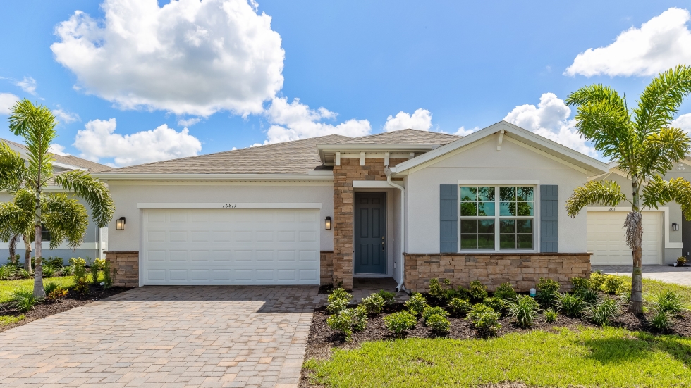Outside of the Clifton model B. Light home with two car garage, one window with shutters, and front door. Mixed paver driveway.