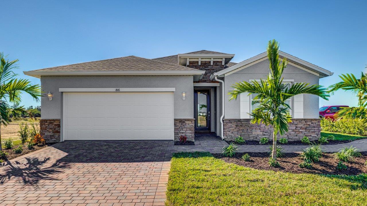 Outside of the Delray model. Grey home with two car garage, window with shutters, and front door. Mixed pavers driveway.