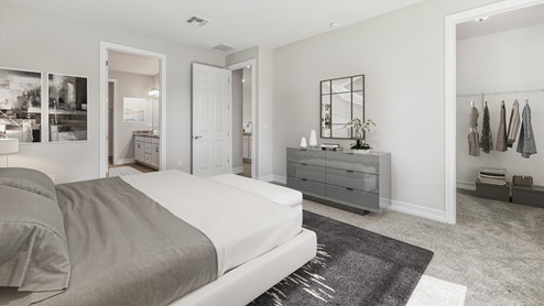 Inside the Clifton primary bedroom with grey walls and grey carpet. You can see into the closet and master bathroom from this angle. There is a dresser next to the door to the living are.