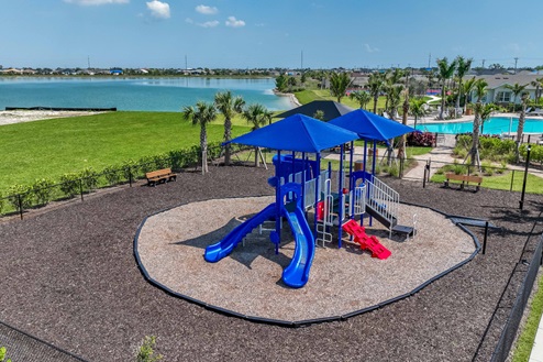Arial view of the playground with slides, climbing options, and interactive toys. Surrounded by mulch, seating options, and gated in.
