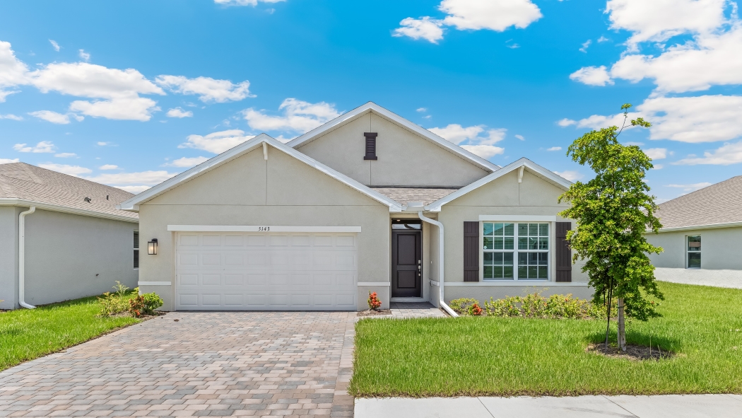 Outside of the Cali D model. Grey home with a two car garage, one window with shutters, and front door. Mixed pavers driveway.