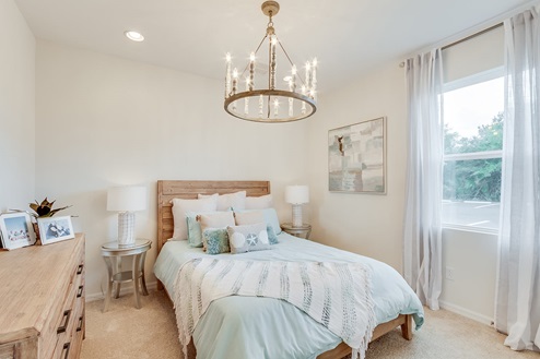 Inside of the Kellen model bedroom one. Crème carpet and white walls. Room contains a bed with nightstands on either side, dresser, and window.
