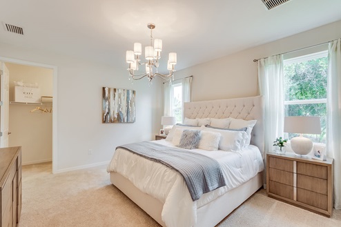 Inside of the Kellen model bedroom one. Crème carpet and white walls. Room contains a bed with nightstands on either side, dresser, and window. Room also has a walk-in closet.