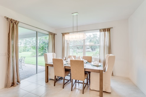 Inside of the Kellen model dining room. Tile flooring and white walls. Dining room has six-person dining table and overhead lighting. In the background there is the glass door that leads to the back patio.